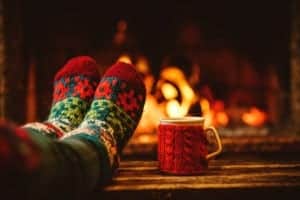 Feet in woolen socks relaxing in front of the fireplace with a mug.