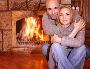 A couple embracing in front of their cabin's fireplace.