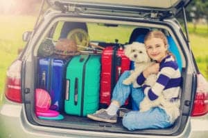 A girl holding her dog in the back of a car filled with suitcases.