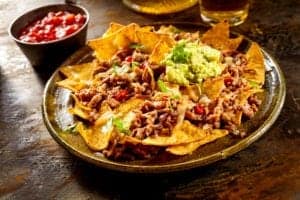 A plate of nachos with ground beef and guacamole.