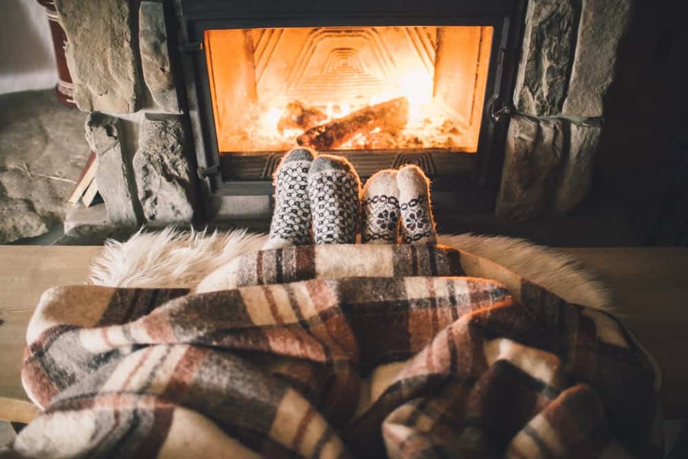 Couple's feet resting by the fireplace under a blanket